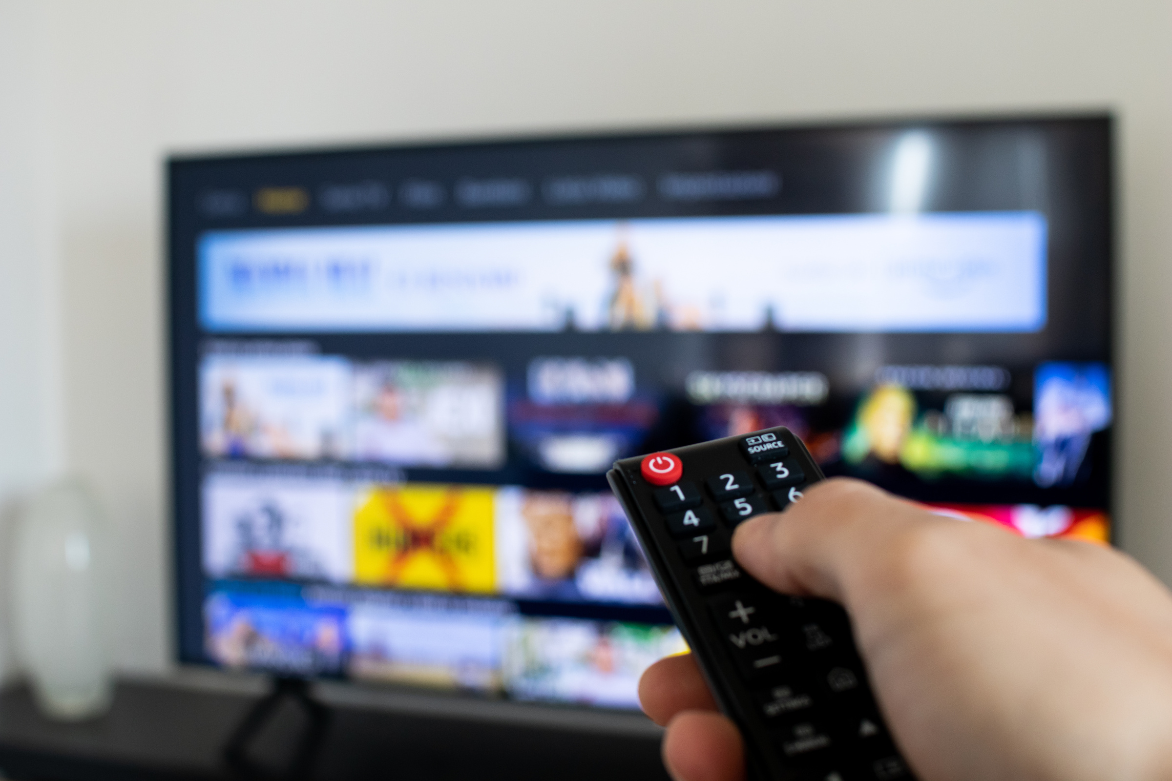 Dłoń z pilotem w dłoni na tle telewizora z wyświetlonymi ikonkami.