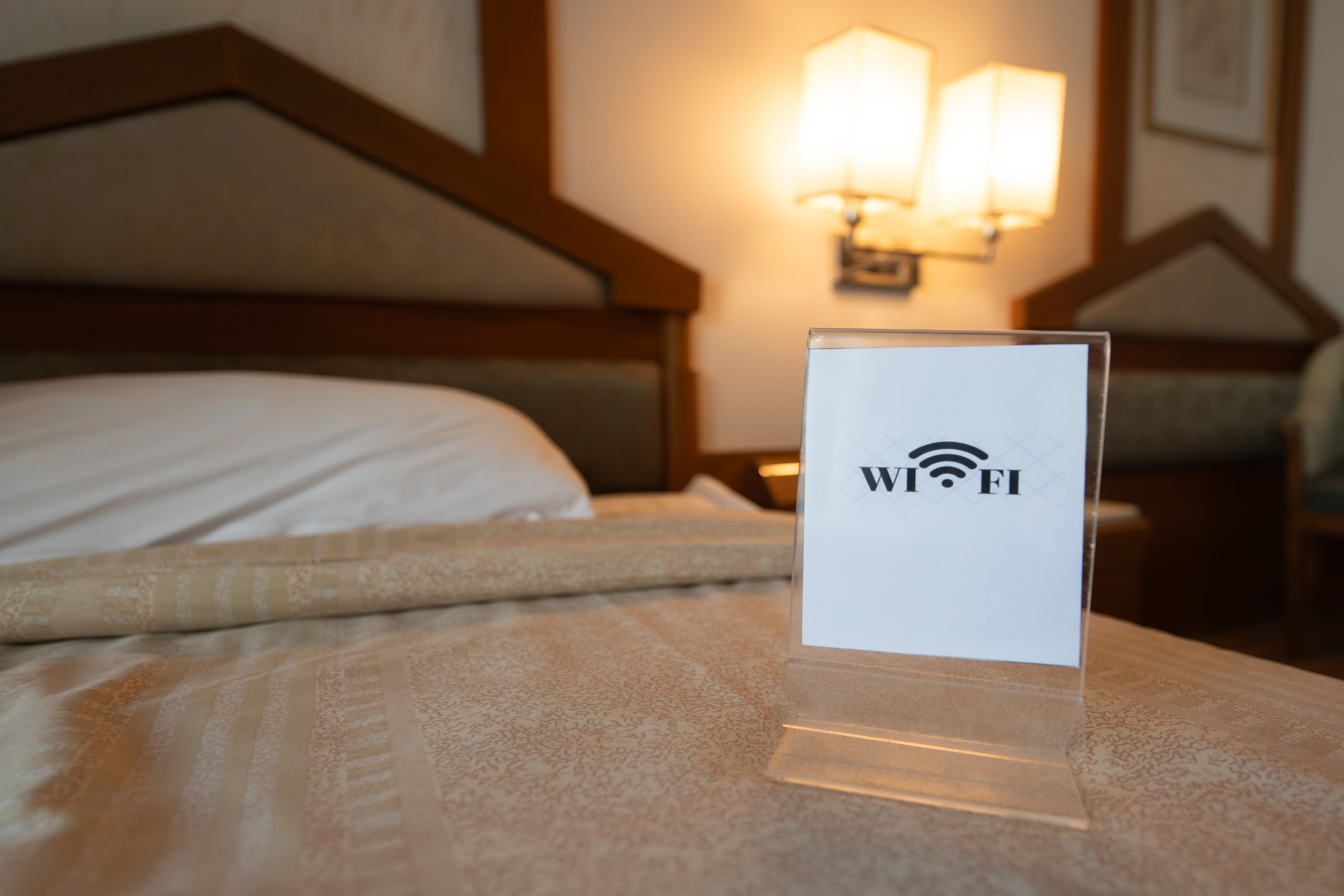 Znaczek wifi z podpisem w standzie stojącym na łóżku w hotelowym pokoju.