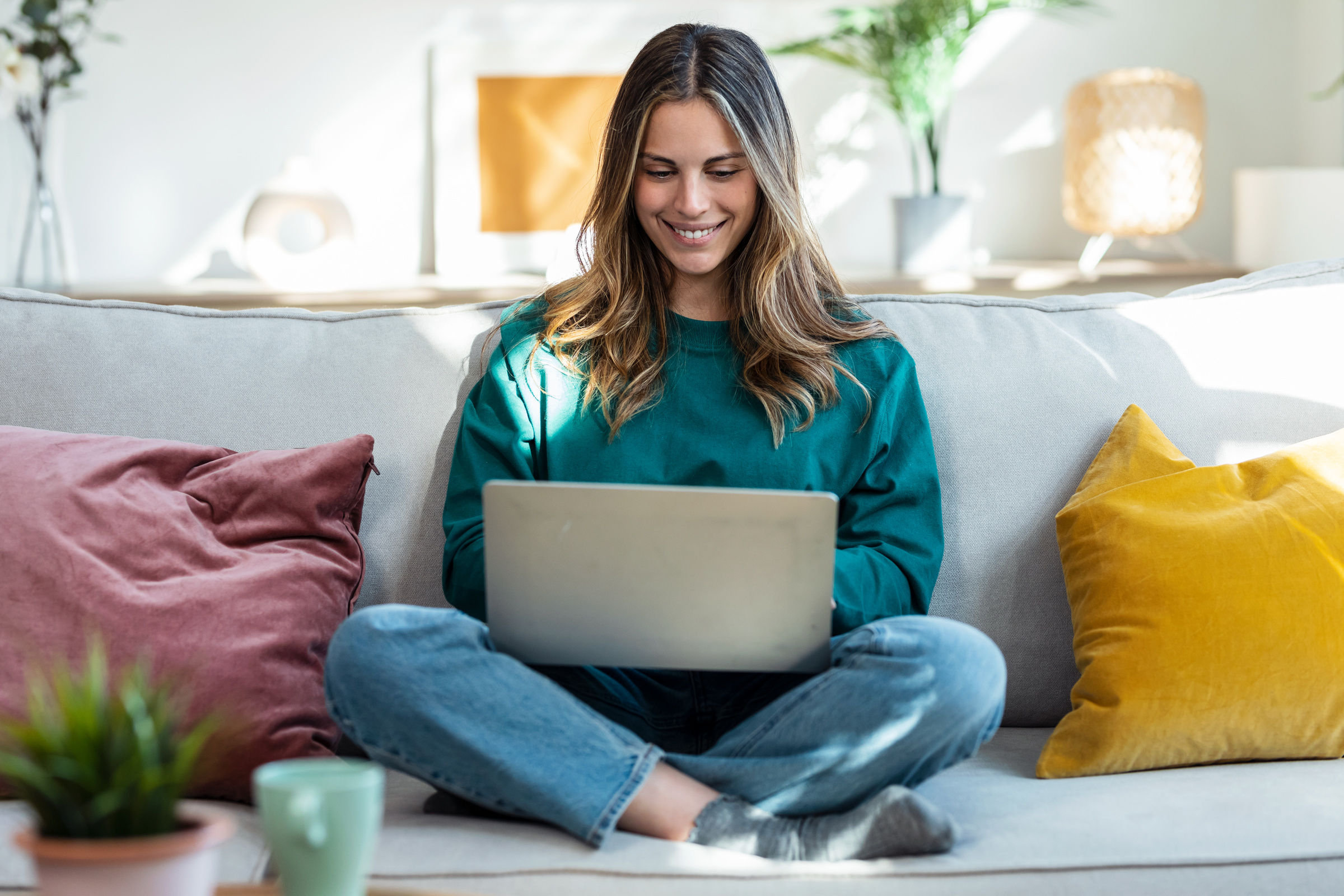 Młoda uśmiechnięta kobieta siedzi na kanapie i korzysta z laptopa z Windows Home
