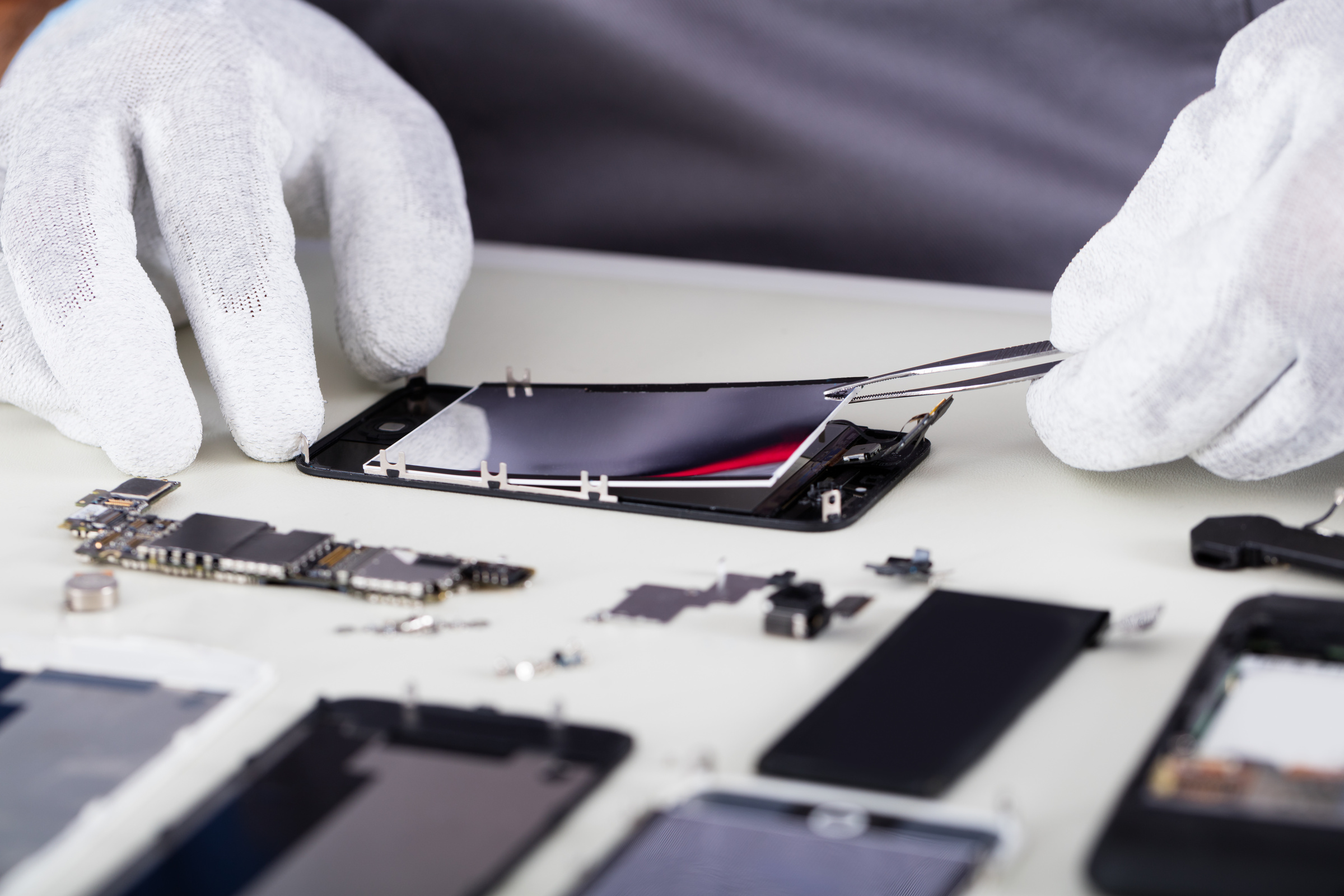Smartfon rozebrany na części przy użyciu pęsety i białych rękawiczek