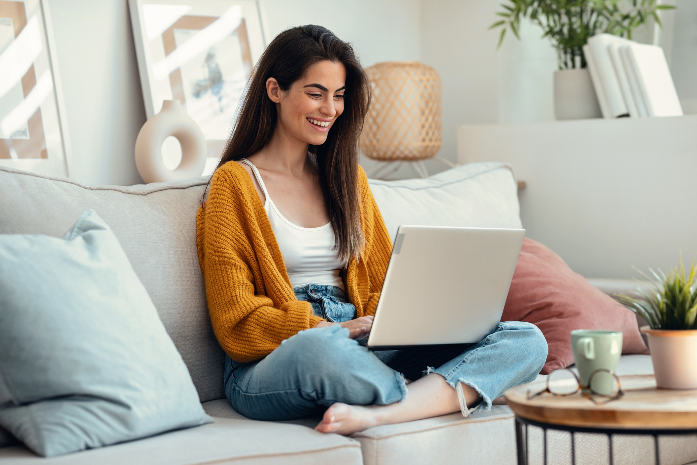 Uśmiechnięta kobieta siedzi na kanapie i korzysta z laptopa z internetem na kartę
