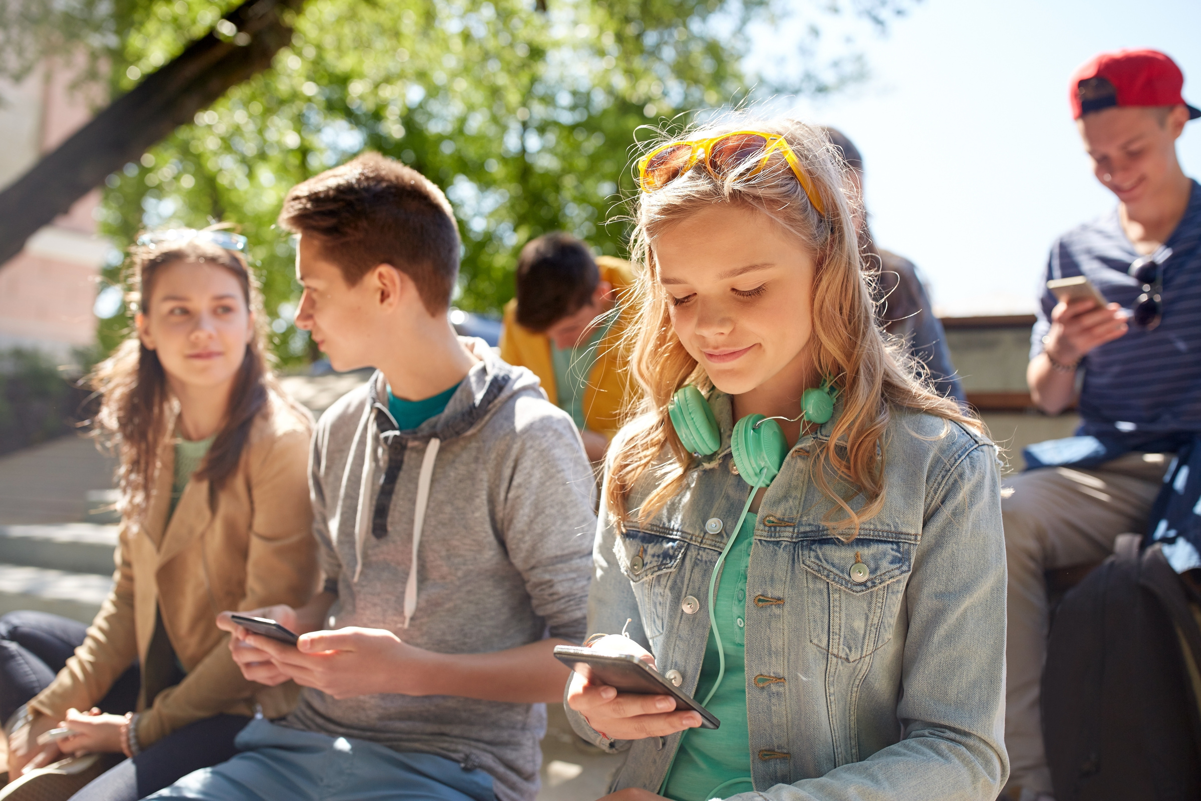 Grupa uczniów siedzi na zewnątrz i korzysta ze smartfonów z internetem na kartę