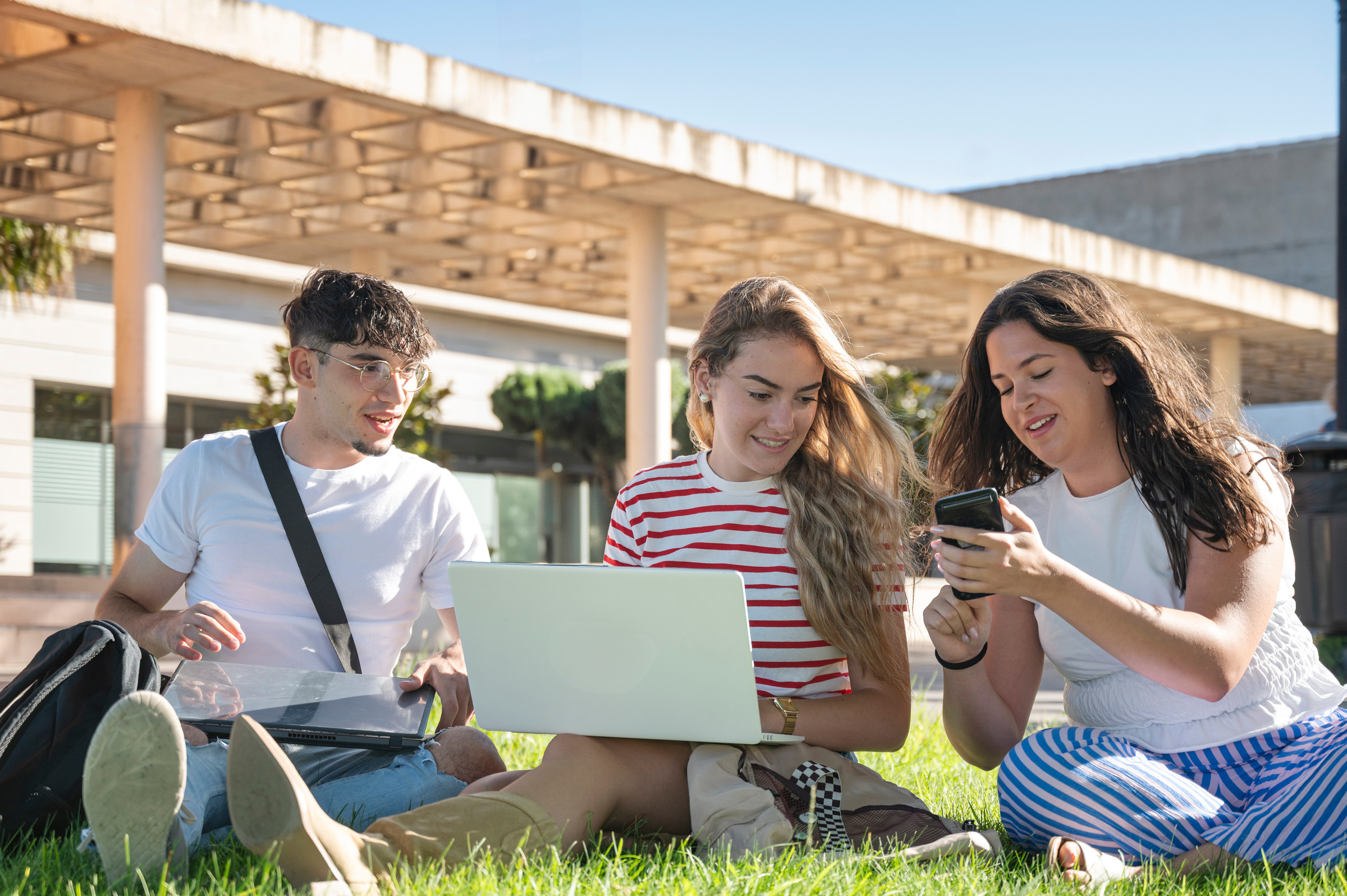 Trzech studentów siedzi na trawie, korzystając z laptopa i smartfona z internetem na kartę