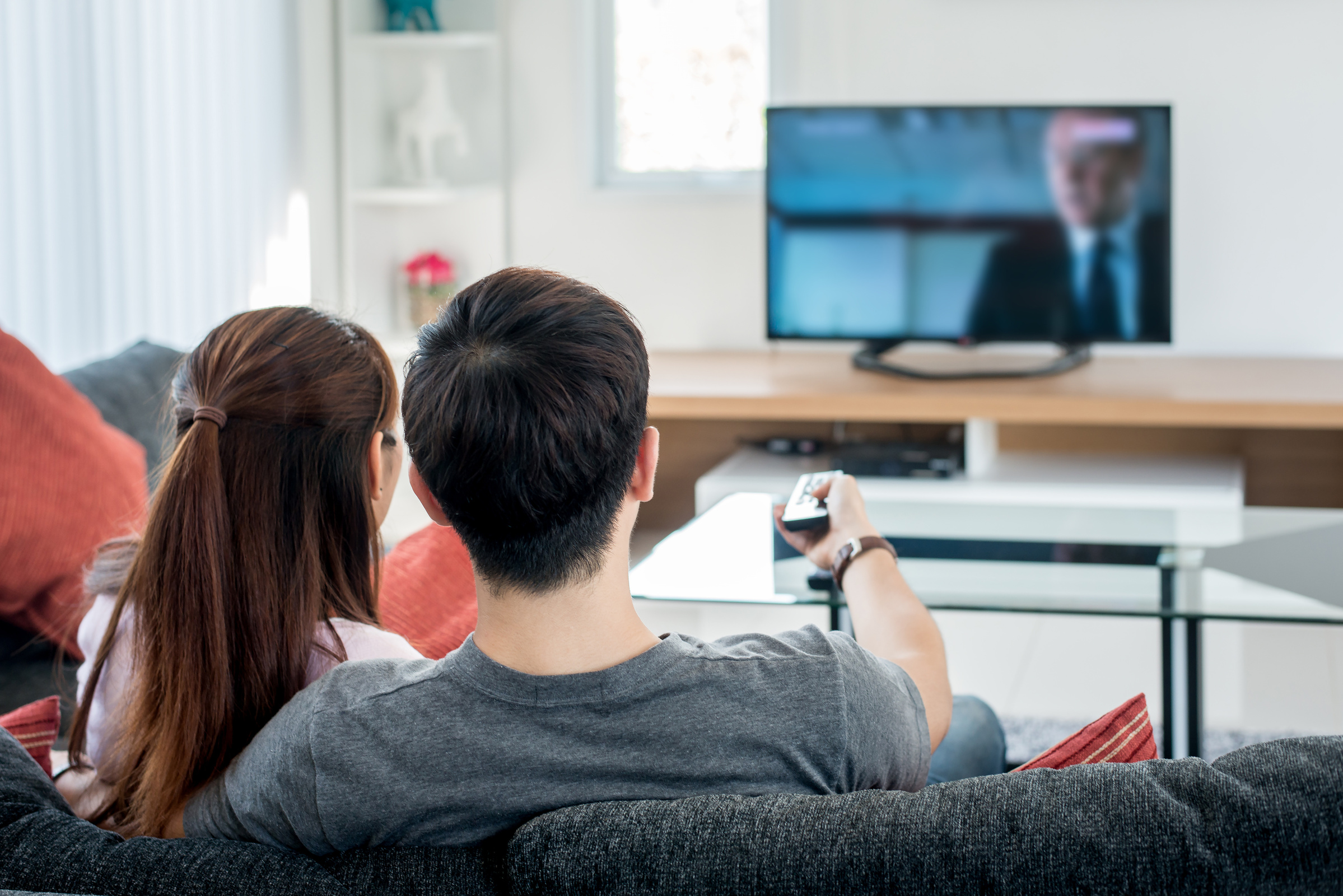 Para siedzi na kanapie przed telewizorem, mężczyzna trzyma w ręku pilot i cofa program w telewizji