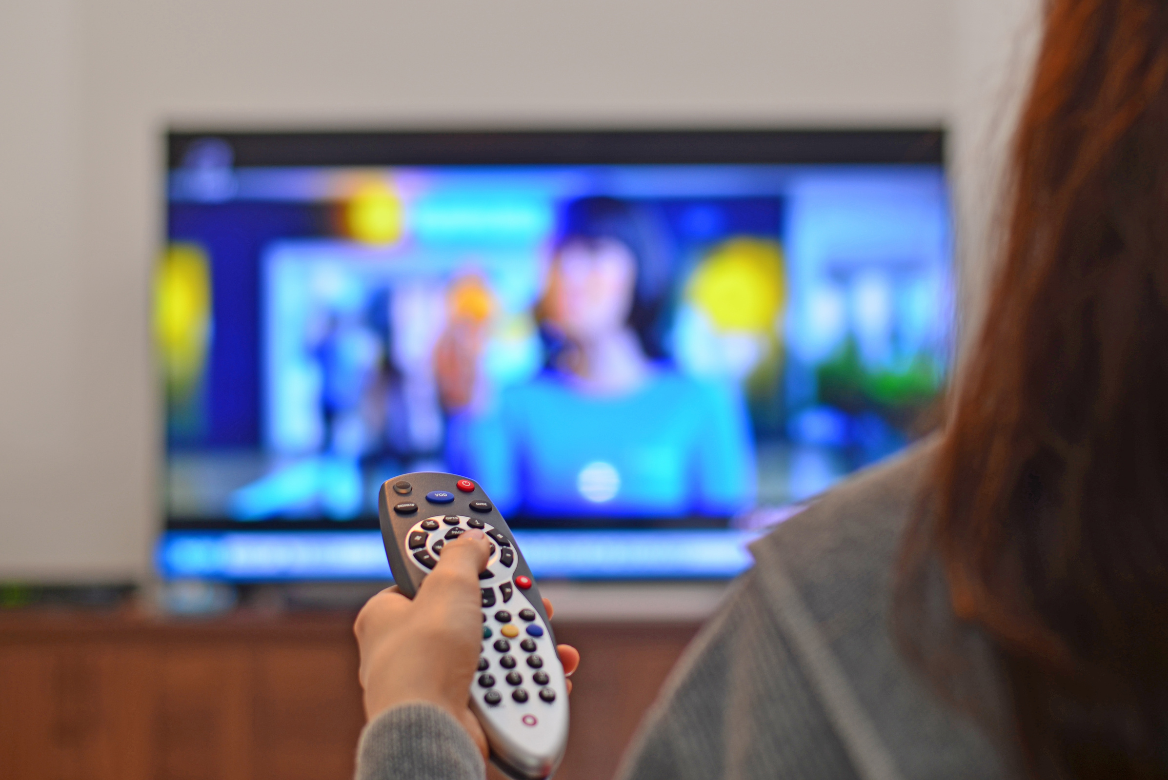 Kobieta trzyma w ręku pilota i cofa program w telewizji, w tle widać niewyraźny ekran