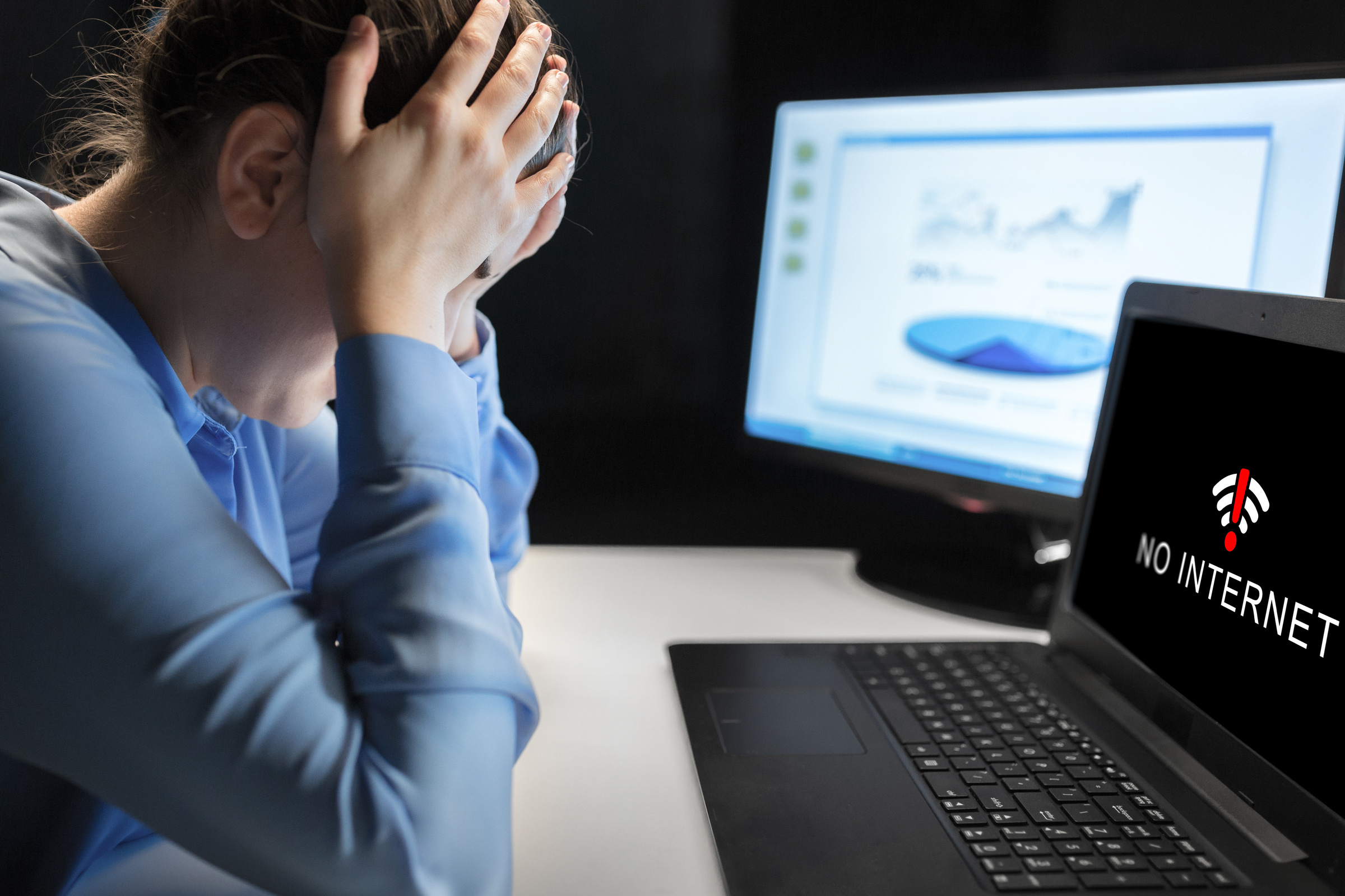 Zdenerwowana kobieta siedzi przy biurku, na ekranie jej laptopa widać komunikat o braku internetu