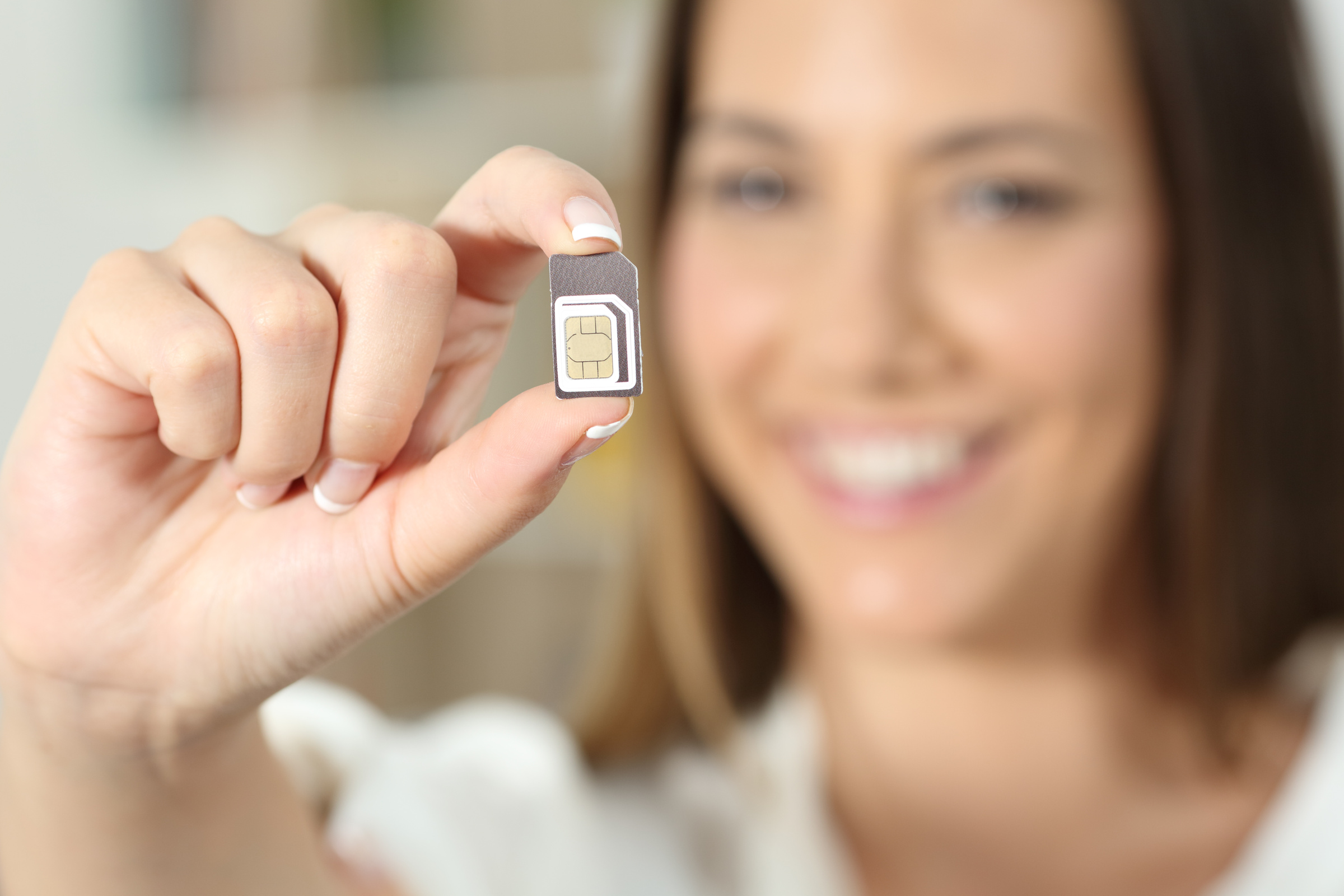 Uśmiechnięta kobieta trzyma w dwóch palcach kartę SIM. 