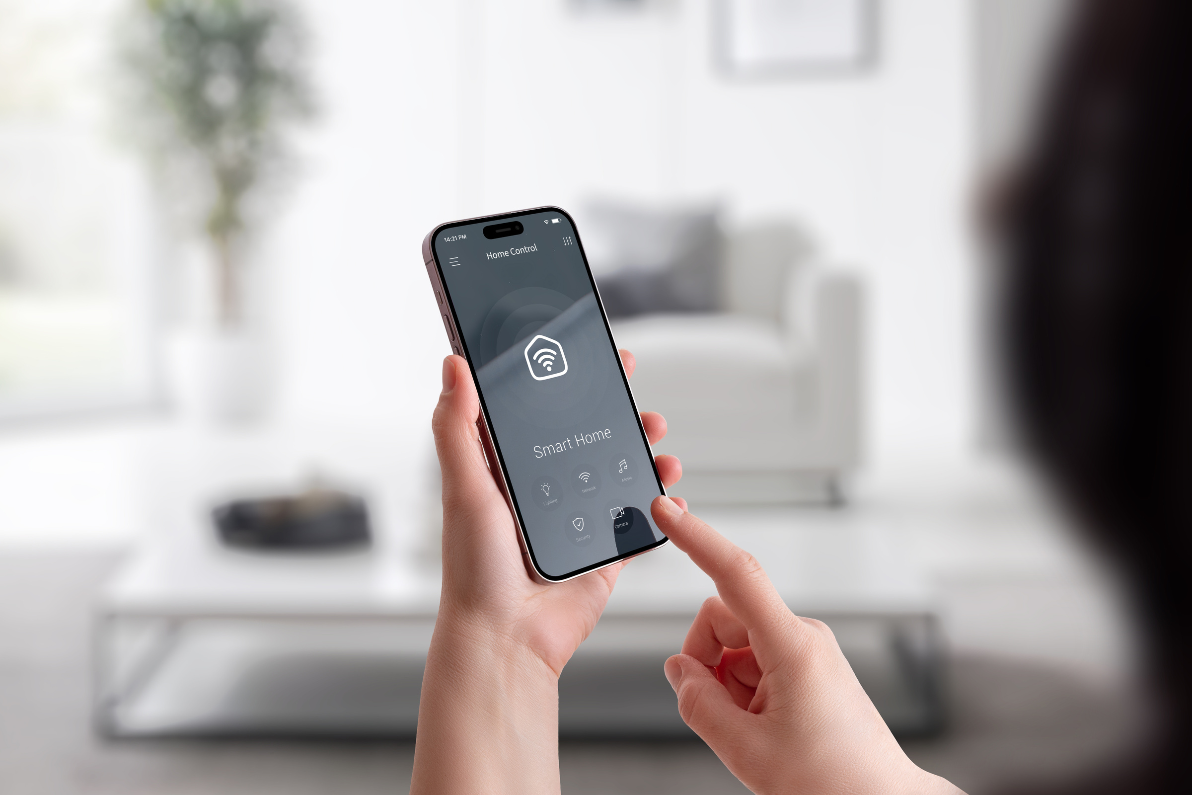 Kobieta stoi w domu i trzyma w lewej ręce smartfon z uruchomioną aplikacją do zarządzania smart home, prawą ręką chce wybrać jedną z opcji.