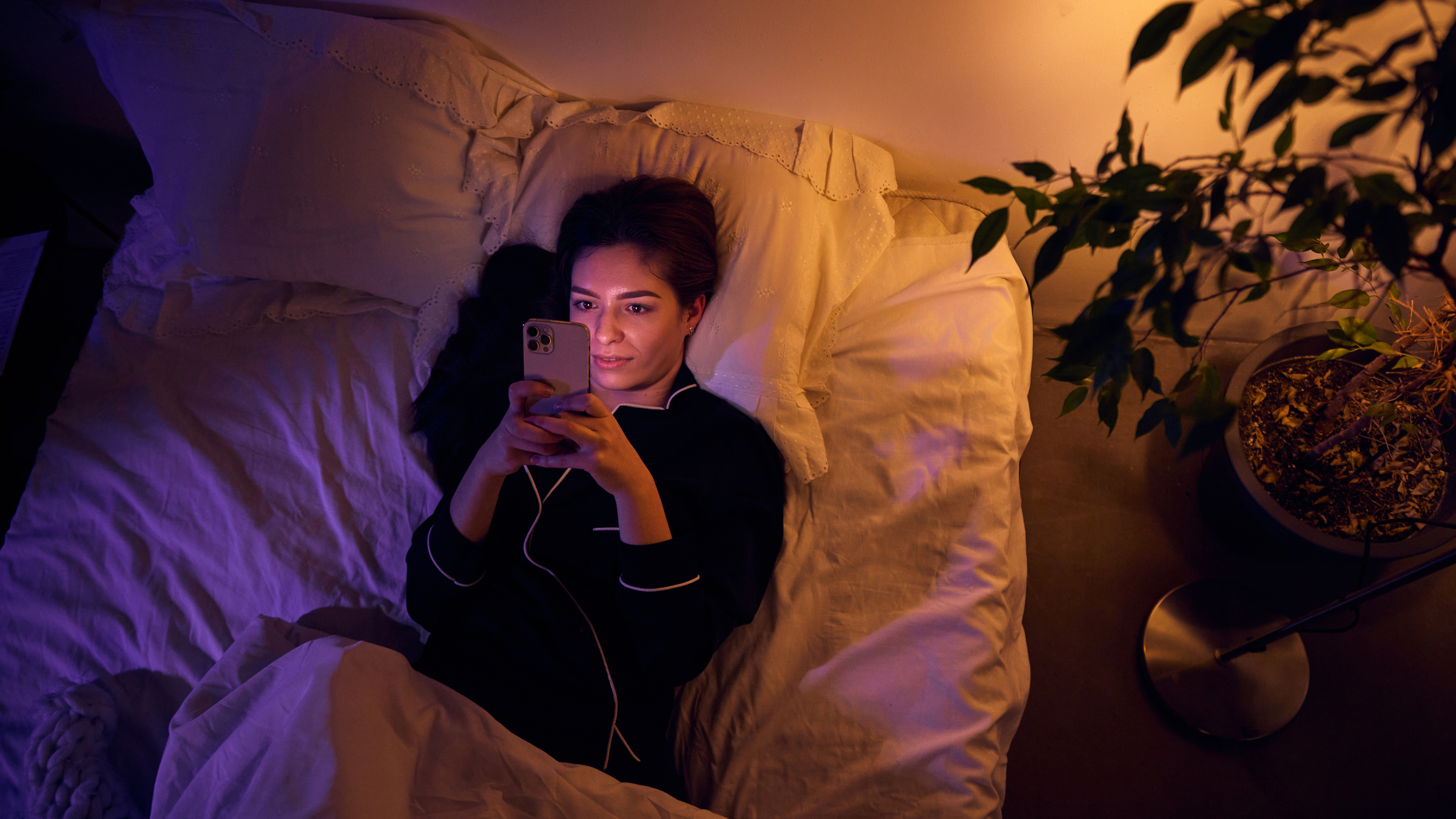 Kobieta korzysta przed snem ze smartfona z włączonym filtrem światła niebieskiego