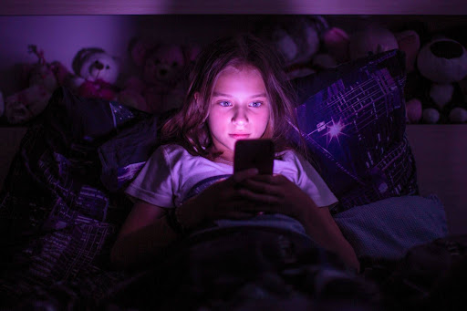 Dziewczynka korzystająca z telefonu w nocy przy zgaszonym świetle.