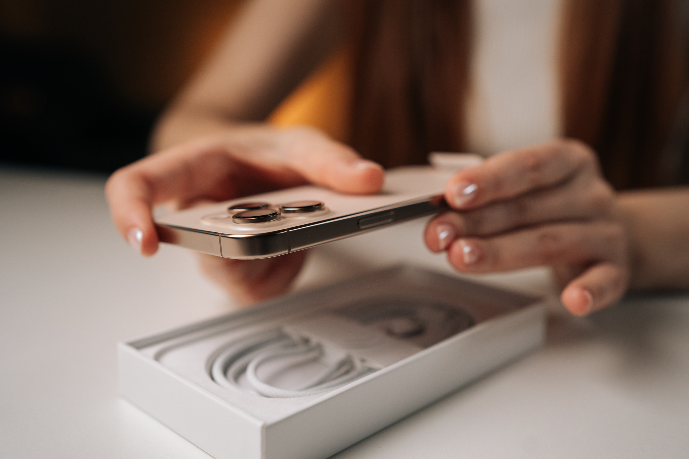 Kobieta wyjmująca nowy telefon iPhone w kolorze złotym z pudełka